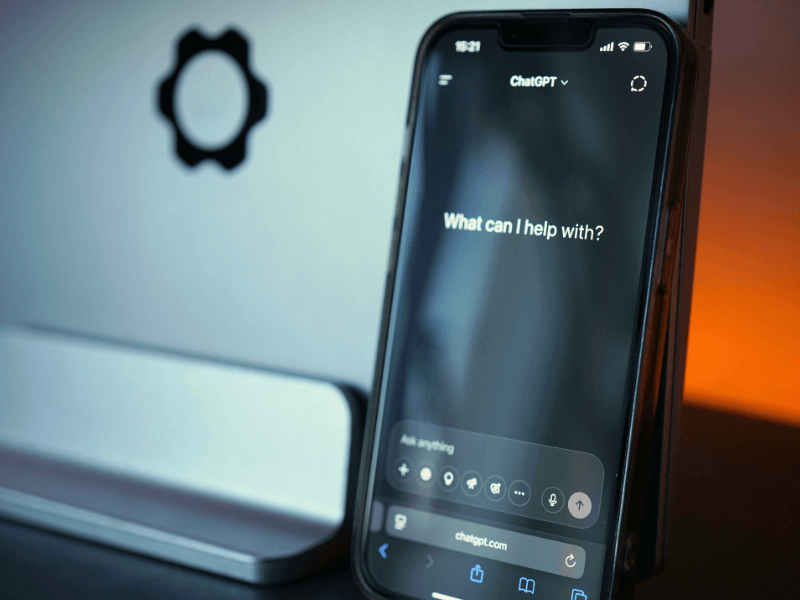 Smartphone displaying the ChatGPT interface in front of a computer monitor, representing AI-powered search and business discovery.